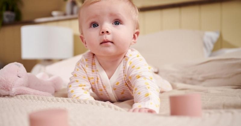 Một em bé sơ sinh đang ngủ yên bình trong cũi, căn phòng có vẻ ấm áp và thoải mái, ánh sáng dịu nhẹ.